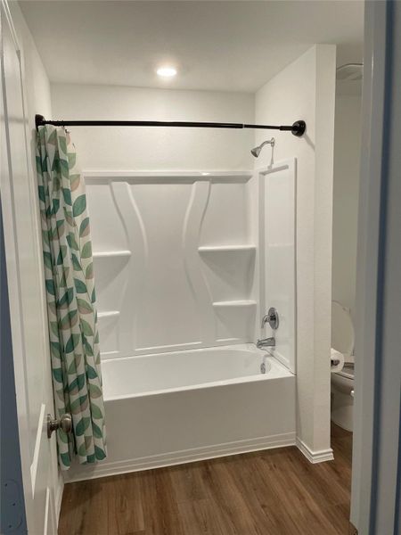 Bathroom featuring dark wood-type flooring and shower / bathtub combination with curtain