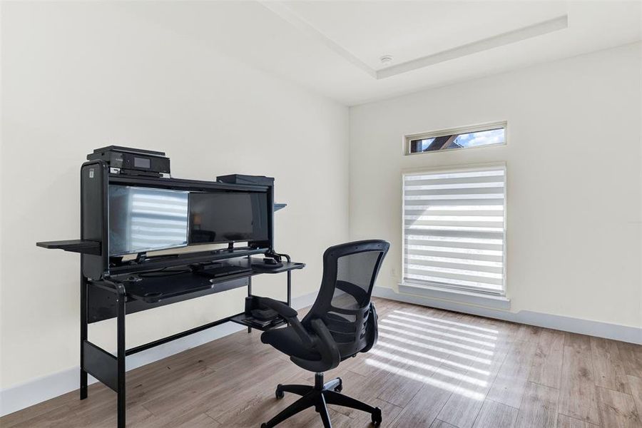 Office area with light wood-style flooring and a raised ceiling Office area with light wood-style flooring and a raised ceiling