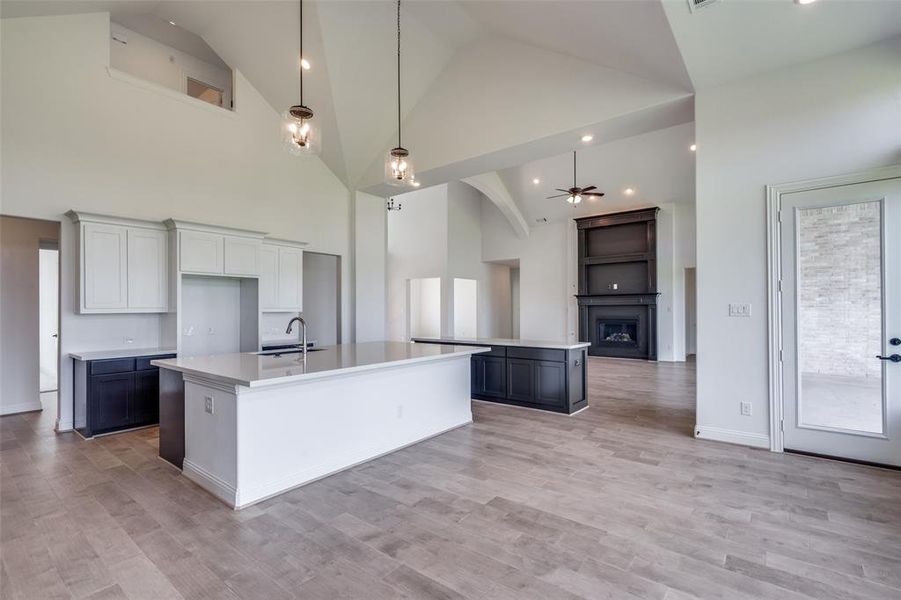 Kitchen featuring high vaulted ceiling, a kitchen island with sink, light wood-type flooring, and hanging light fixtures