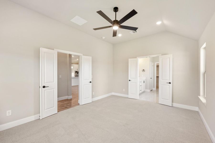 Bedroom with vaulted ceiling, ceiling fan, carpet flooring, and doors leading to ensuite bathroom and walk-in closet Bedroom with vaulted ceiling, ceiling fan, carpet flooring, and doors leading to ensuite bathroom and walk-in closet