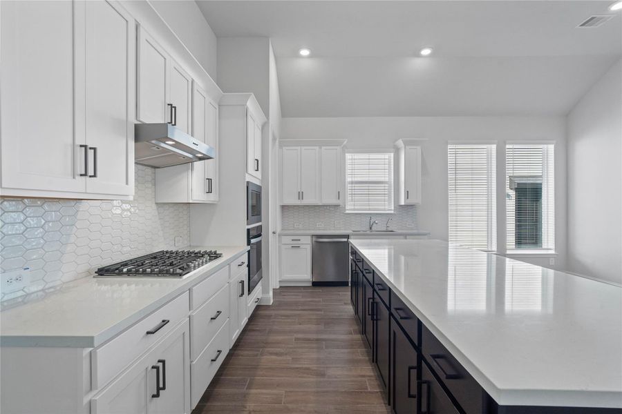 The open-concept gourmet kitchen designed for both cooking and entertaining. It features elegant white shaker-style cabinetry, pristine quartz countertops, and a large central island that doubles as a functional breakfast bar. The cooking area is a chef's dream with a sleek stainless steel gas cooktop, hood vent, wall oven and microwave, all complemented by a chic tile backsplash. The open-concept gourmet kitchen designed for both cooking and entertaining. It features elegant white shaker-style cabinetry, pristine quartz countertops, and a large central island that doubles as a functional breakfast bar. The cooking area is a chef's dream with a sleek stainless steel gas cooktop, hood vent, wall oven and microwave, all complemented by a chic tile backsplash.