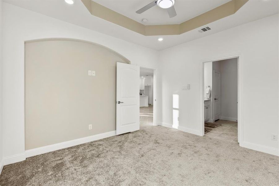 Unfurnished bedroom with connected bathroom, a raised ceiling, light carpet, and ceiling fan