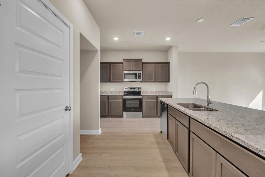 Kitchen featuring appliances with stainless steel finishes, recessed lighting, dark brown cabinetry, light stone countertops, and light wood-style floors