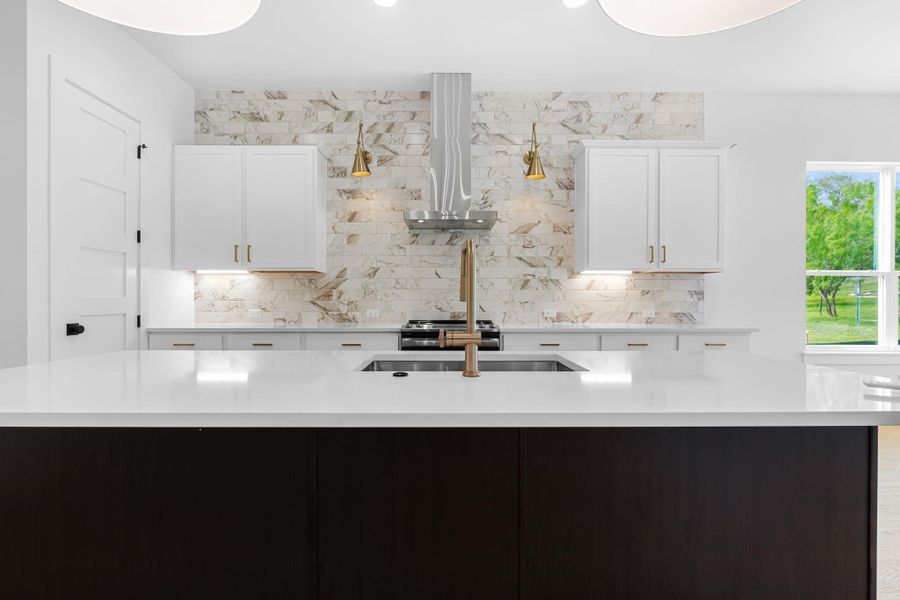 Kitchen featuring white cabinetry, tasteful backsplash, an island with sink, and wall chimney exhaust hood Kitchen featuring white cabinetry, tasteful backsplash, an island with sink, and wall chimney exhaust hood
