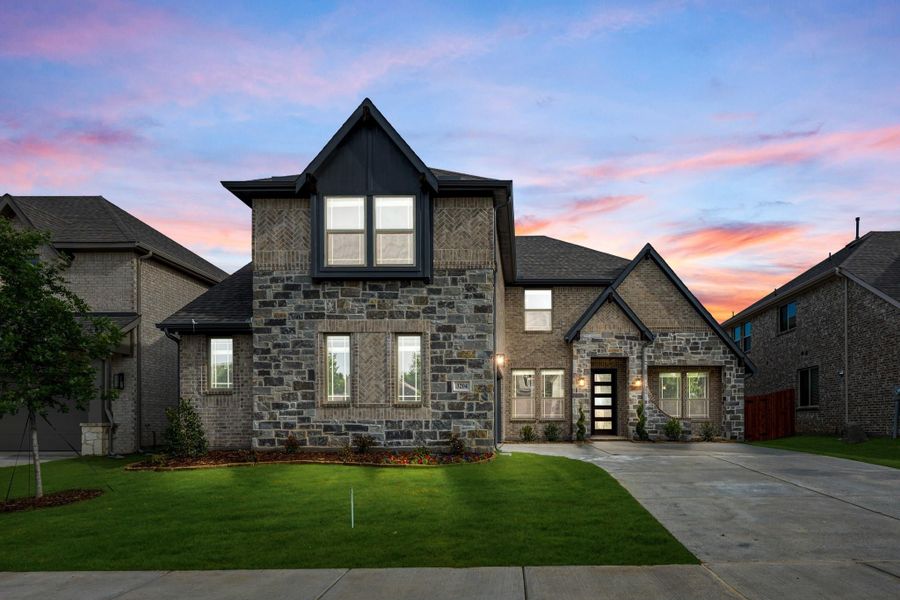 Two-story home with stone and brick exterior, dark roof, and concrete driveway at dusk Two-story home with stone and brick exterior, dark roof, and concrete driveway at dusk