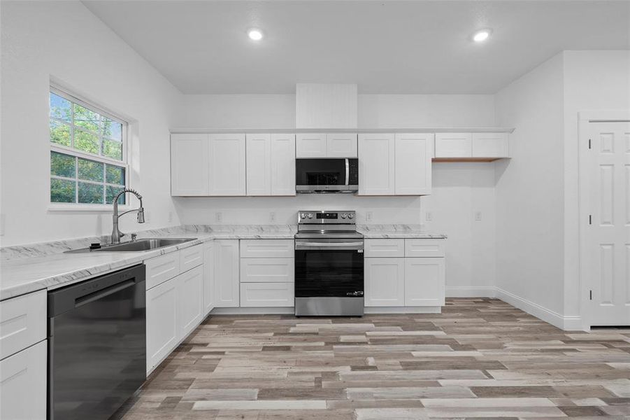 Kitchen featuring appliances with stainless steel finishes, white cabinets, light wood-type flooring, light stone countertops, and recessed lighting
