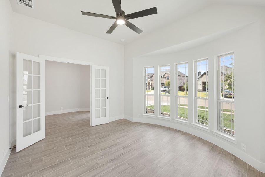 Bright empty room with French doors, ceiling fan, and a row of large windows overlooking a neighborhood