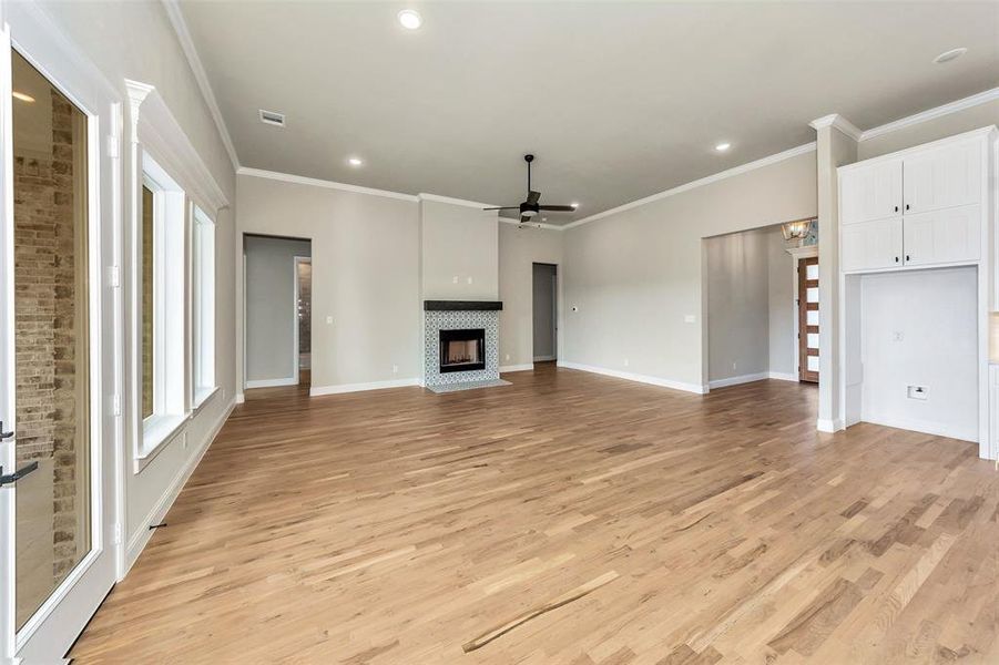 Unfurnished living room featuring ornamental molding, a fireplace, ceiling fan, and light wood-type flooring