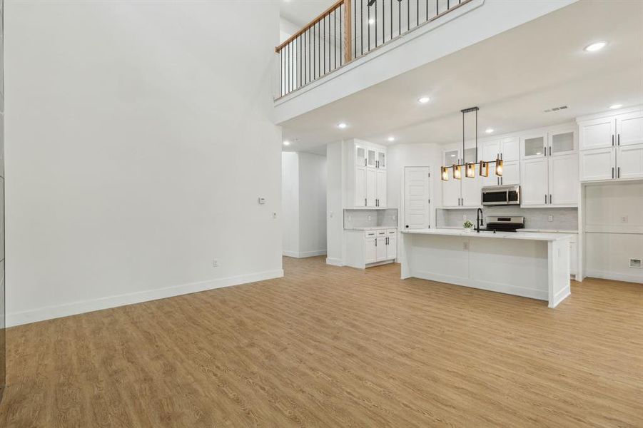 Kitchen featuring light wood-type flooring, an island with sink, white cabinets, range, and decorative light fixtures