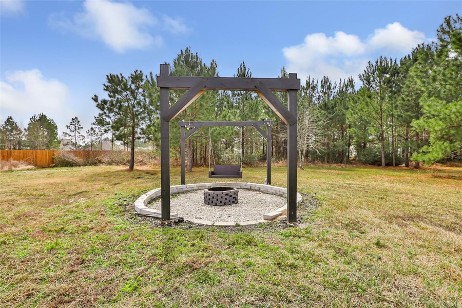 Spacious backyard featuring a cozy fire pit with surrounding swings, perfect for relaxation and gatherings, set against a backdrop of lush trees for privacy.