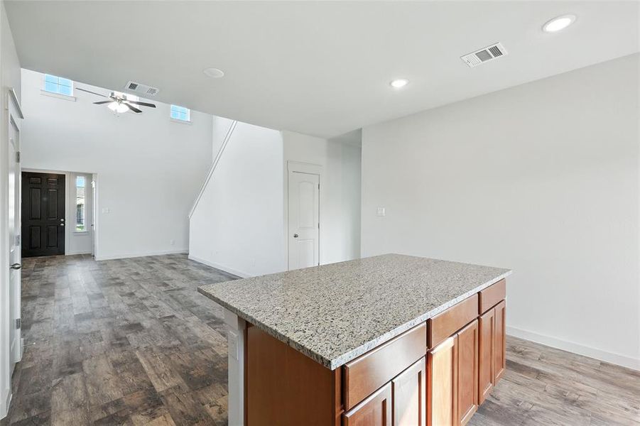 Kitchen featuring brown cabinetry, light stone countertops, a ceiling fan, a center island, and light wood-type flooring Kitchen featuring brown cabinetry, light stone countertops, a ceiling fan, a center island, and light wood-type flooring