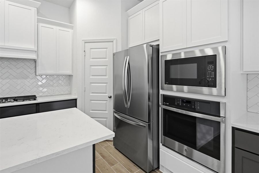 Modern kitchen with sleek stainless steel appliances, elegant white cabinetry, and a stylish herringbone backsplash.