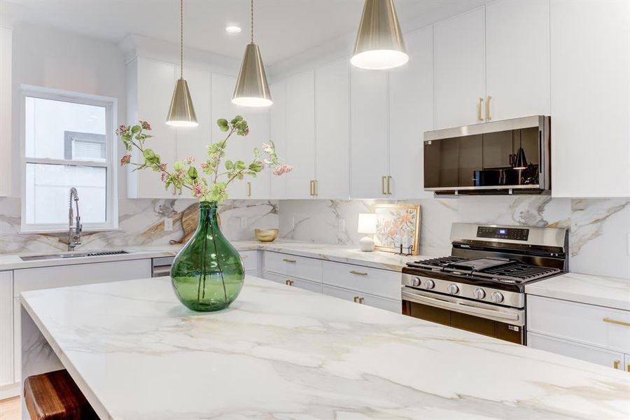 This stunning kitchen features gold hardware, quartz countertops, gas range, and stainless steel appliances. There is plenty of storage space in the cabinets.