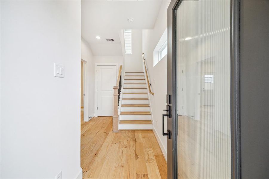 Modern entryway with natural wood flooring and a staircase leading to the upper level. The space is illuminated by recessed lighting and a narrow window, creating an inviting atmosphere.