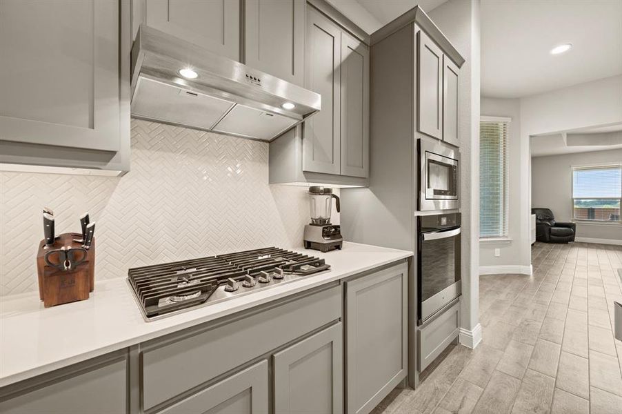 Sleek kitchen detail showcasing the built-in gas cooktop, modern vent hood, quartz countertops, and a stylish herringbone backsplash.