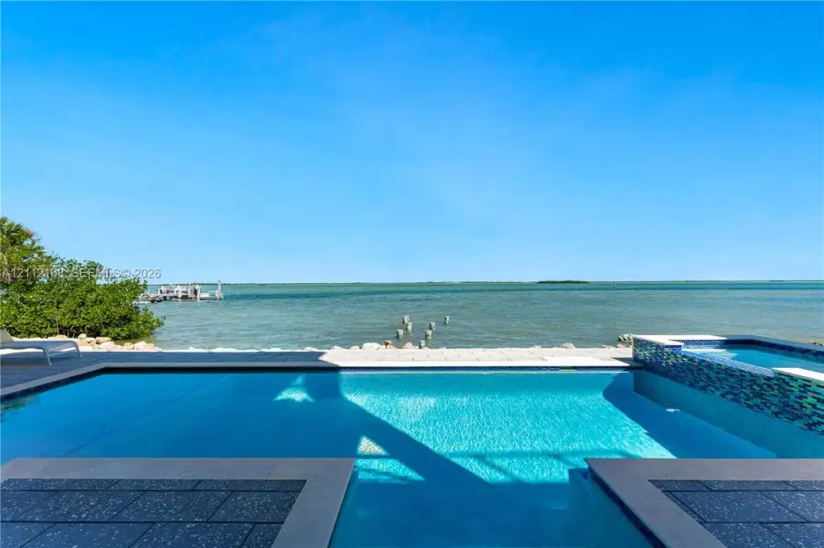 In-ground swimming pool featuring a tiled spillover spa, stone paver decking, and direct water frontage In-ground swimming pool featuring a tiled spillover spa, stone paver decking, and direct water frontage