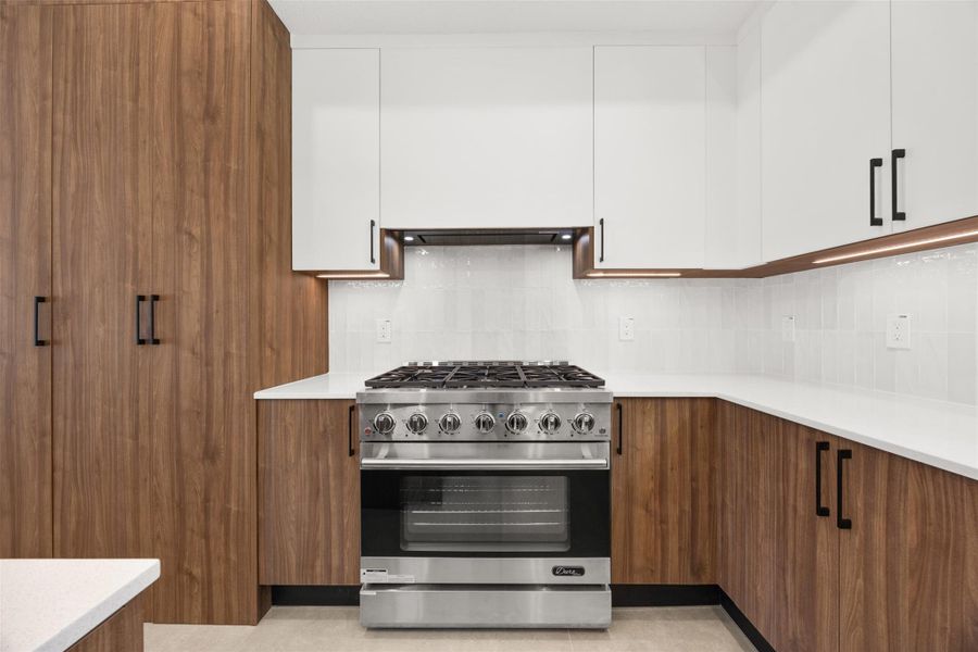 Premium 36-inch gas range surrounded by custom designed cabinetry, quartz countertops, and under-cabinet lighting.