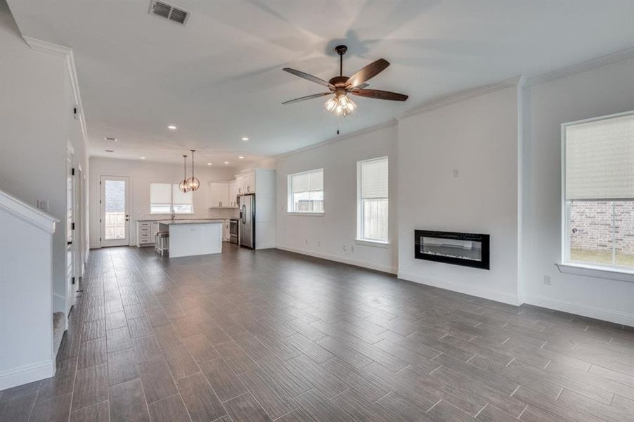 Unfurnished living room featuring ceiling fan with notable chandelier, a healthy amount of sunlight, sink, and crown molding