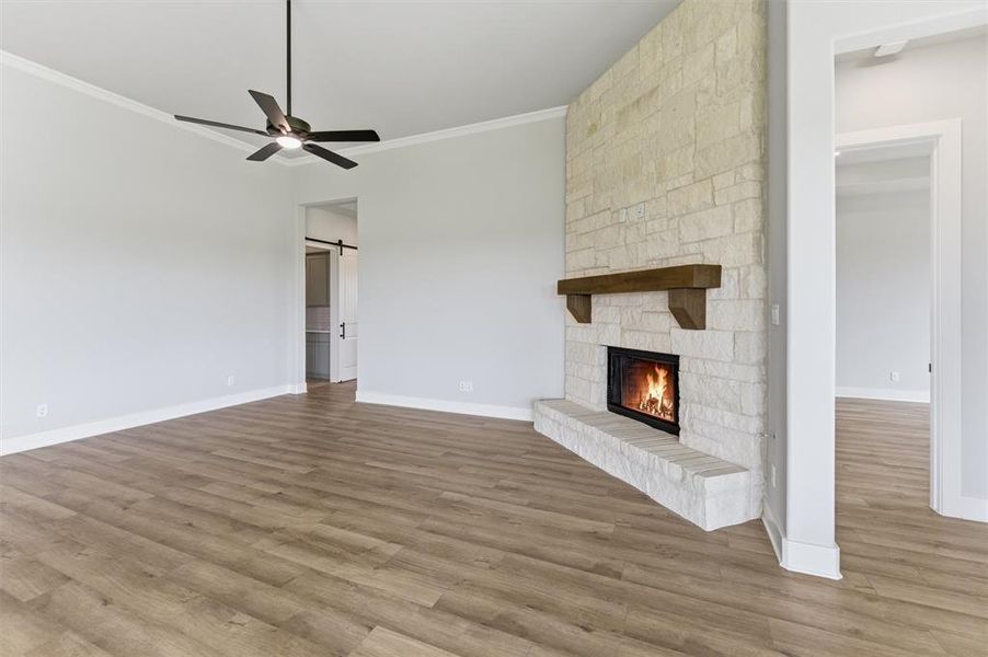 Unfurnished living room with a barn door, wood finished floors, a ceiling fan, and ornamental molding
