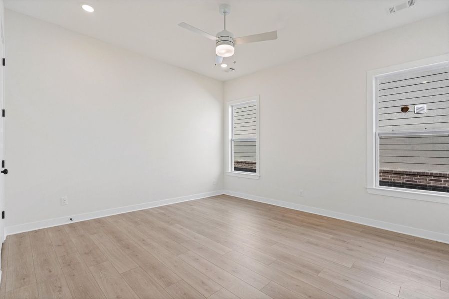 Recessed ceiling lighting, wood-finish flooring, two windows with blinds, a ceiling fan with integrated lighting, and a white interior door with black hardware