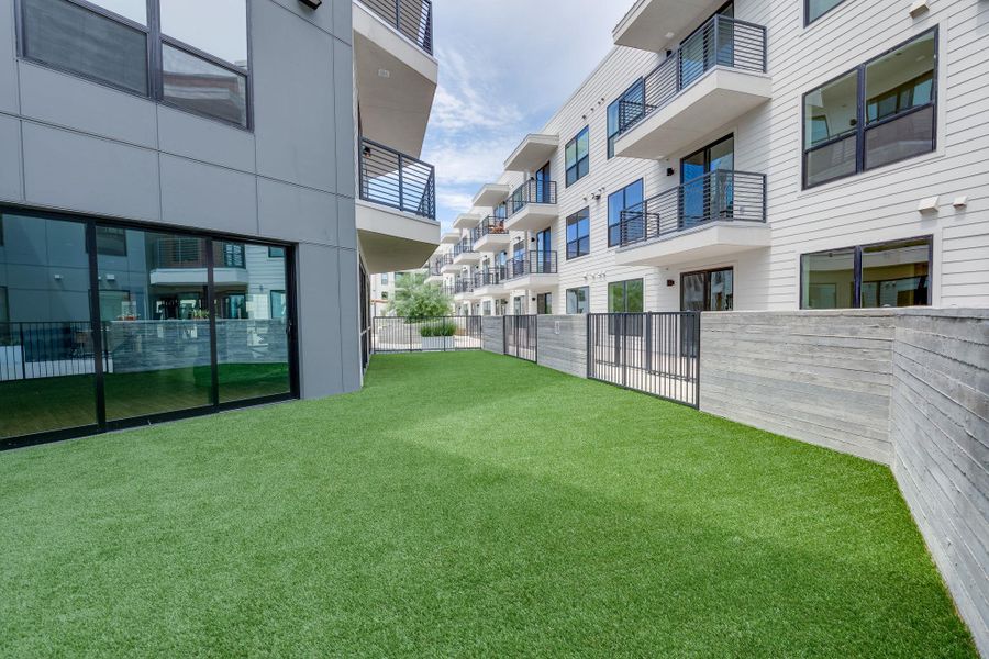 Expansive green space featuring artificial turf, bordered by a concrete retaining wall and a black metal fence