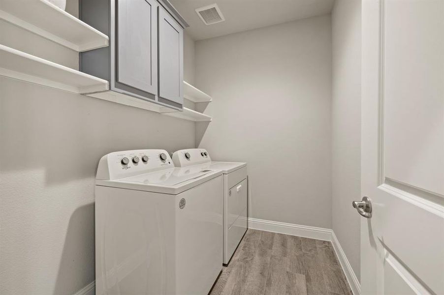 Dedicated laundry room  with space for side-by-side washer and dryer, overhead cabinets, and built-in shelving for organized storage.
