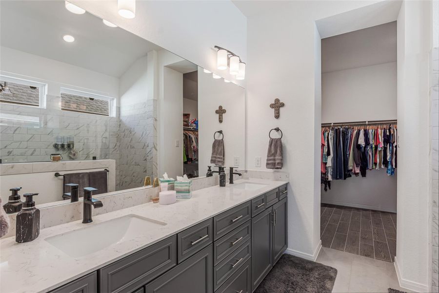 Another view of the bathroom featuring a dual-sink vanity with a quartz countertop, modern fixtures, and ample storage, adjacent to a spacious walk-in closet.