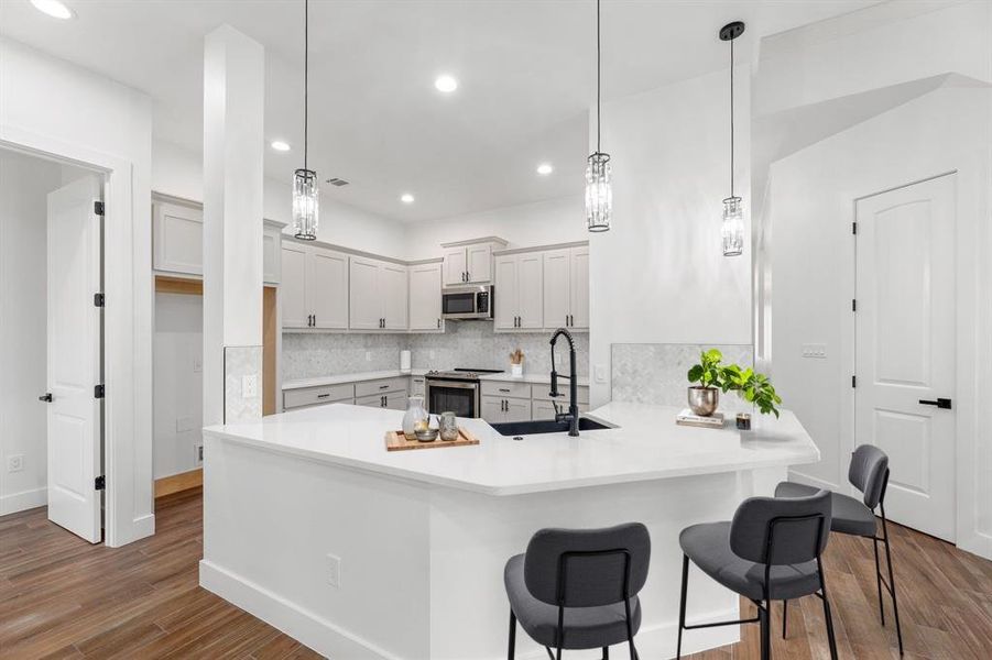 Designer kitchen featuring a sink, dark wood-style floors, stainless steel appliances, a peninsula, and decorative backsplash