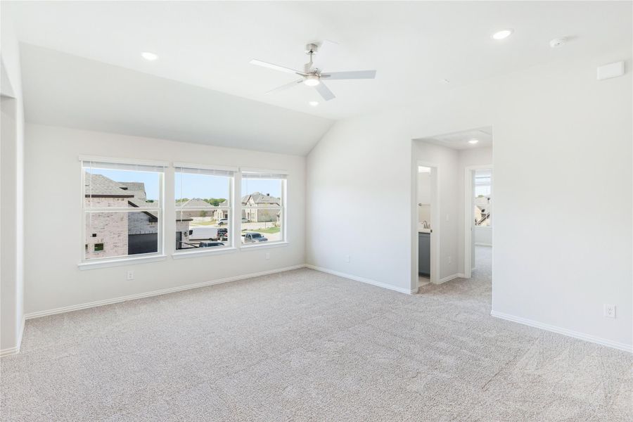 Empty bedroom with vaulted ceiling, ceiling fan, carpet flooring, and large windows overlooking a neighborhood