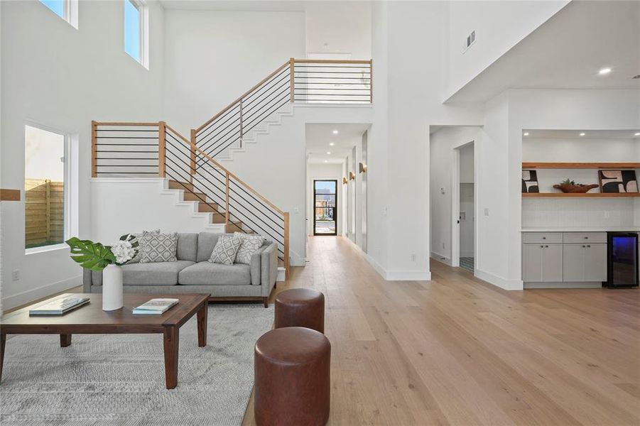 Living room featuring light wood-style flooring, a towering ceiling, wine cooler, stairway, and recessed lighting