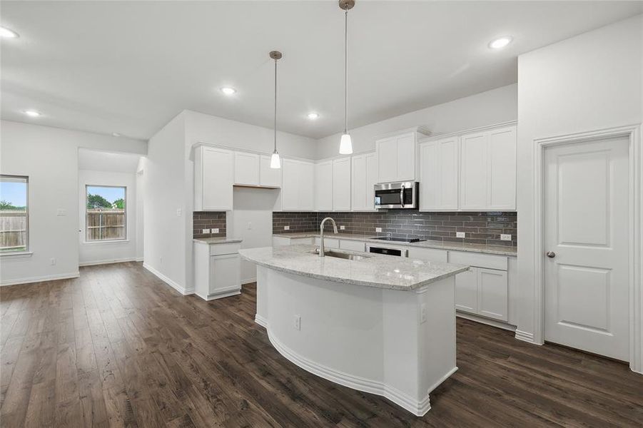 Kitchen featuring a sink, a center island with sink, stainless steel microwave, and backsplash Kitchen featuring a sink, a center island with sink, stainless steel microwave, and backsplash
