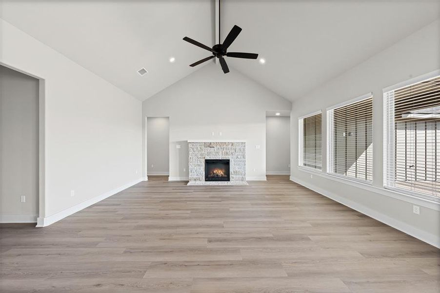 Unfurnished living room featuring light wood-type flooring, high vaulted ceiling, a fireplace, and a ceiling fan