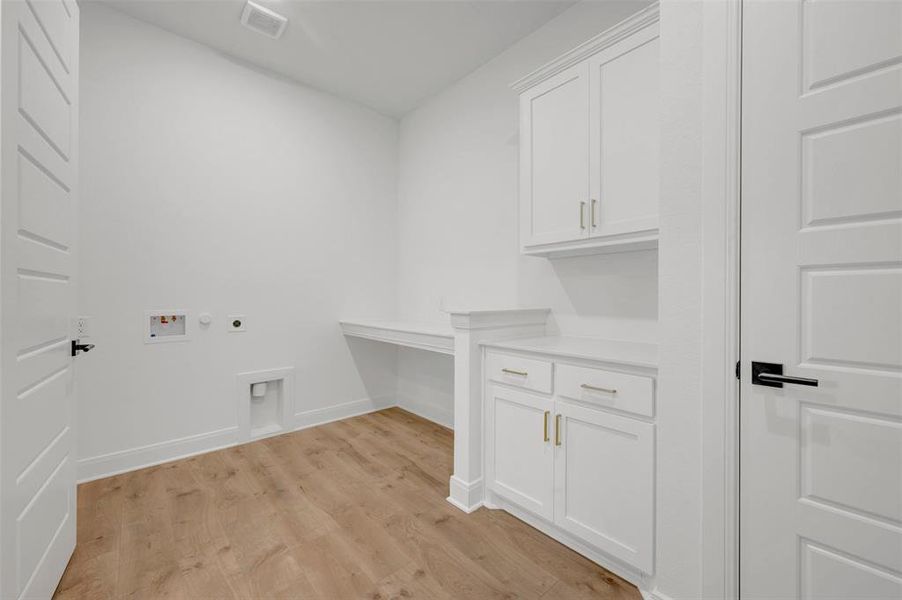 This utility room features light wood-style flooring, white walls, and white cabinetry with gold-toned hardware