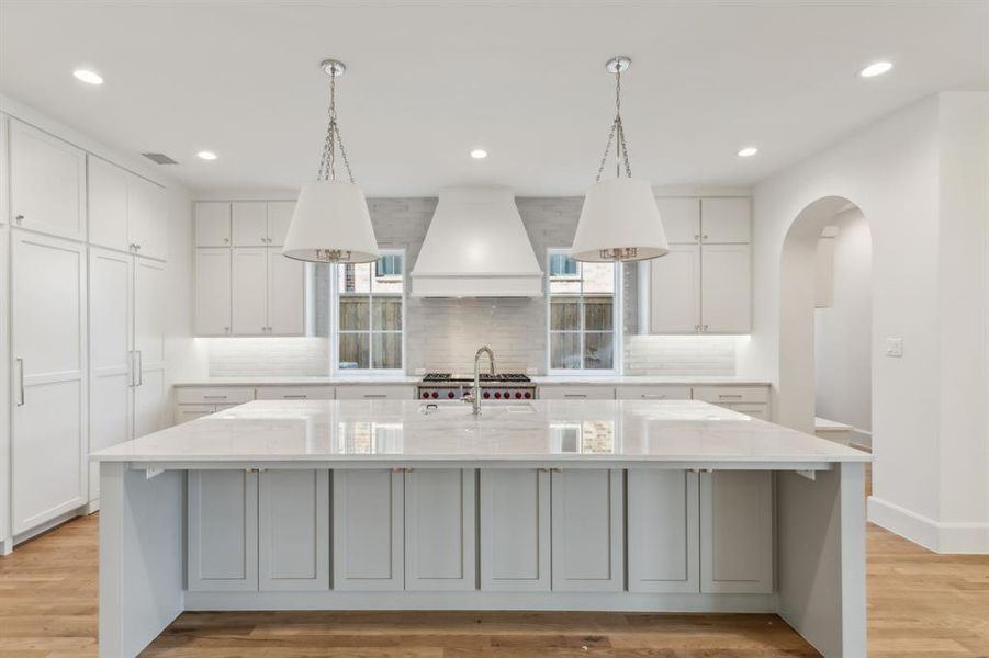 Kitchen featuring a large island, premium range hood, decorative light fixtures, and light hardwood flooring