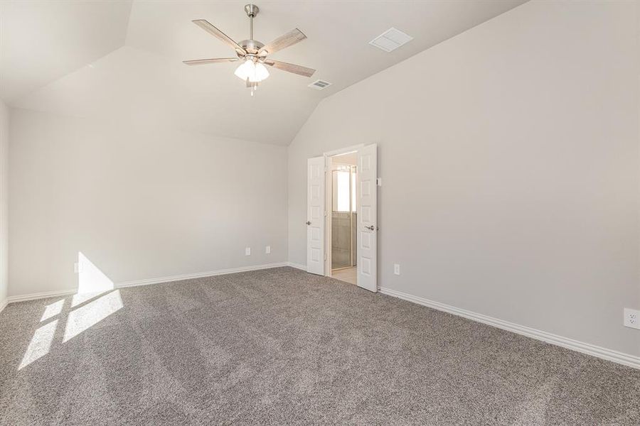 Carpeted spare room featuring vaulted ceiling and ceiling fan