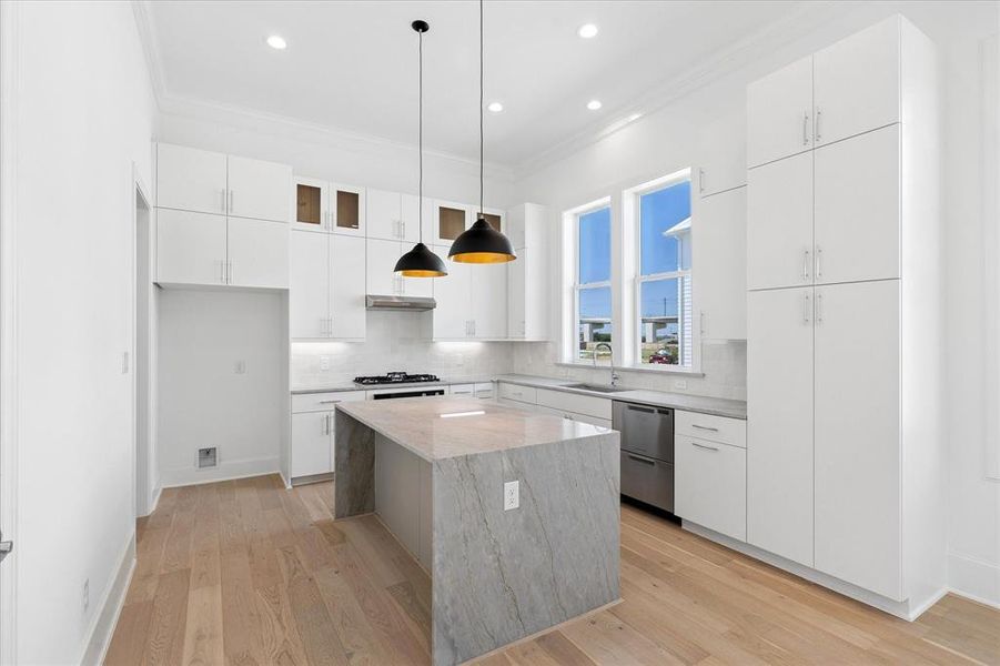 Modern kitchen featuring an expansive center island with waterfall countertop, stainless steel appliances, white cabinetry, and wood-finish flooring