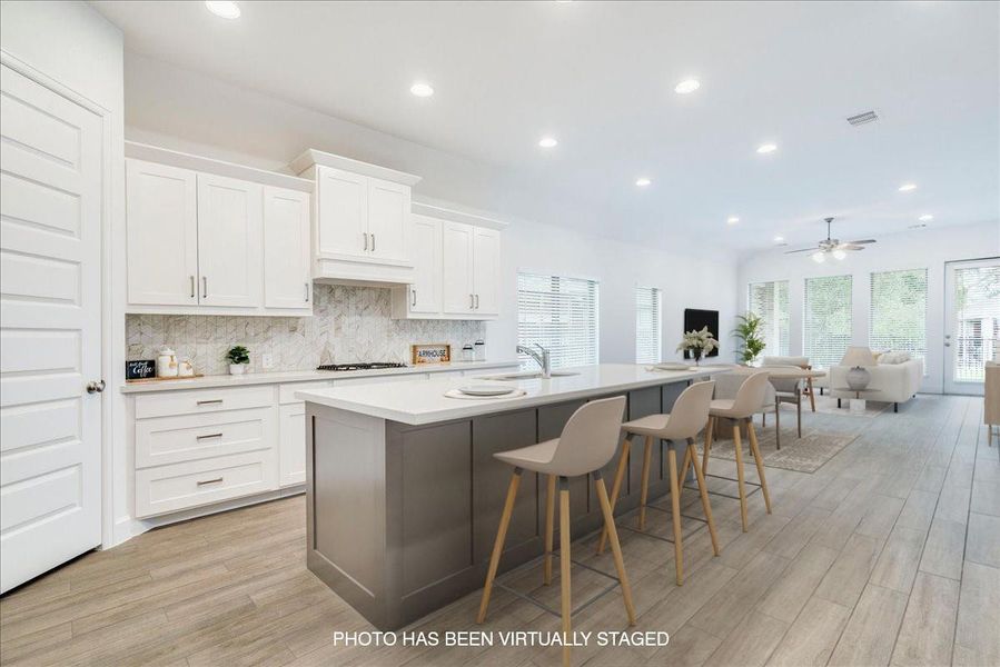Open-concept living area featuring a kitchen with white cabinetry, a spacious island with seating, a white countertop, and light-colored tile flooring
