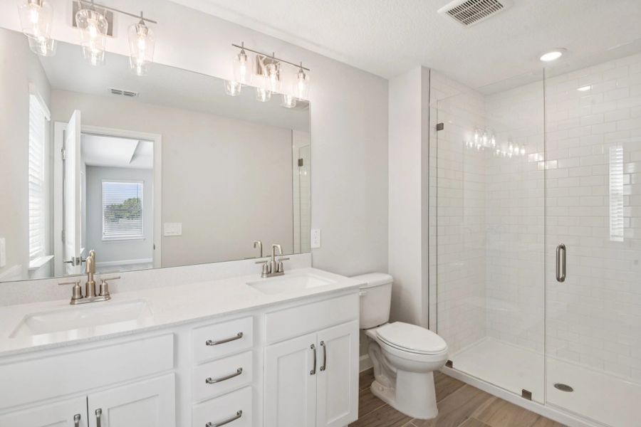 Beautiful primary bathroom with double sinks and a large frameless walk-in shower all with aspects of AW Collection® Timeless