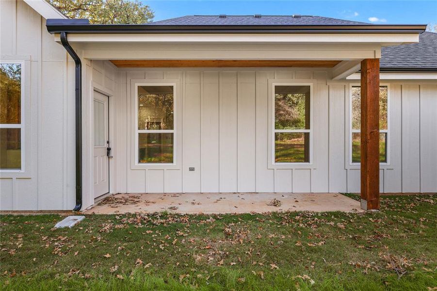 Property entrance with a patio, a lawn, a shingled roof, and board and batten siding