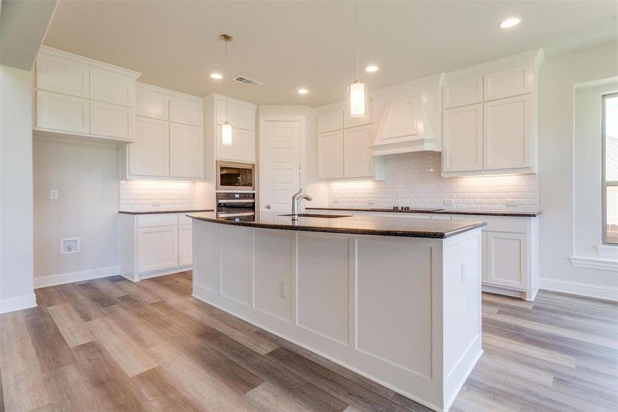 Kitchen featuring tasteful backsplash, a kitchen island with sink, sink, white cabinetry, and light wood-type flooring