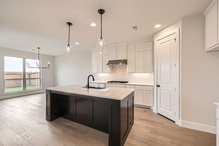 Kitchen featuring backsplash, a sink, gas cooktop, under cabinet range hood, and visible vents Kitchen featuring backsplash, a sink, gas cooktop, under cabinet range hood, and visible vents