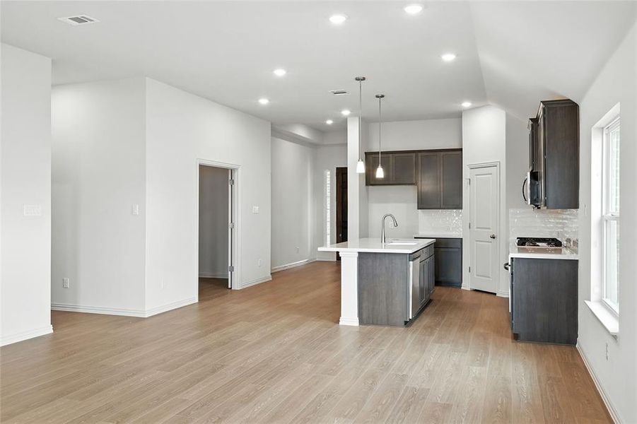 Kitchen featuring tasteful backsplash, a center island with sink, decorative light fixtures, light wood finished floors, and open floor plan Kitchen featuring tasteful backsplash, a center island with sink, decorative light fixtures, light wood finished floors, and open floor plan