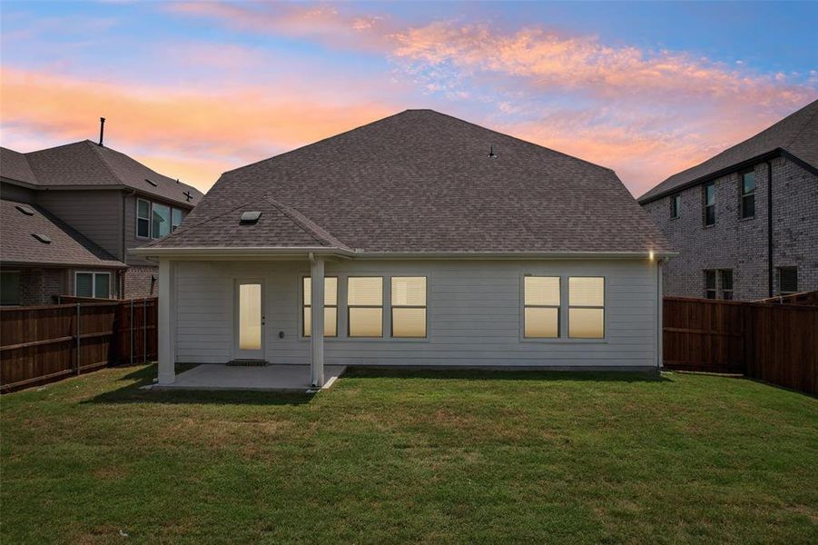 Back house at dusk featuring a patio and a lawn