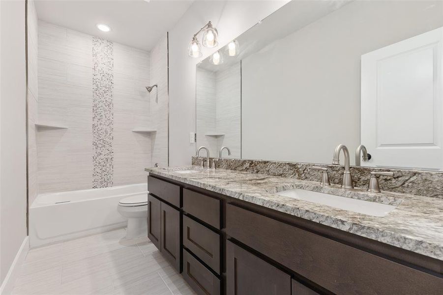 Full bathroom featuring double sink vanity, tiled shower / bath combo, tile patterned flooring, and toilet