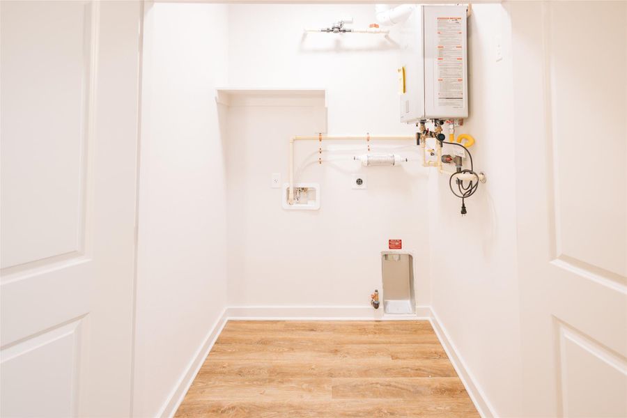 Clothes washing area featuring electric dryer hookup, tankless water heater, light wood-style floors, washer hookup, and baseboards