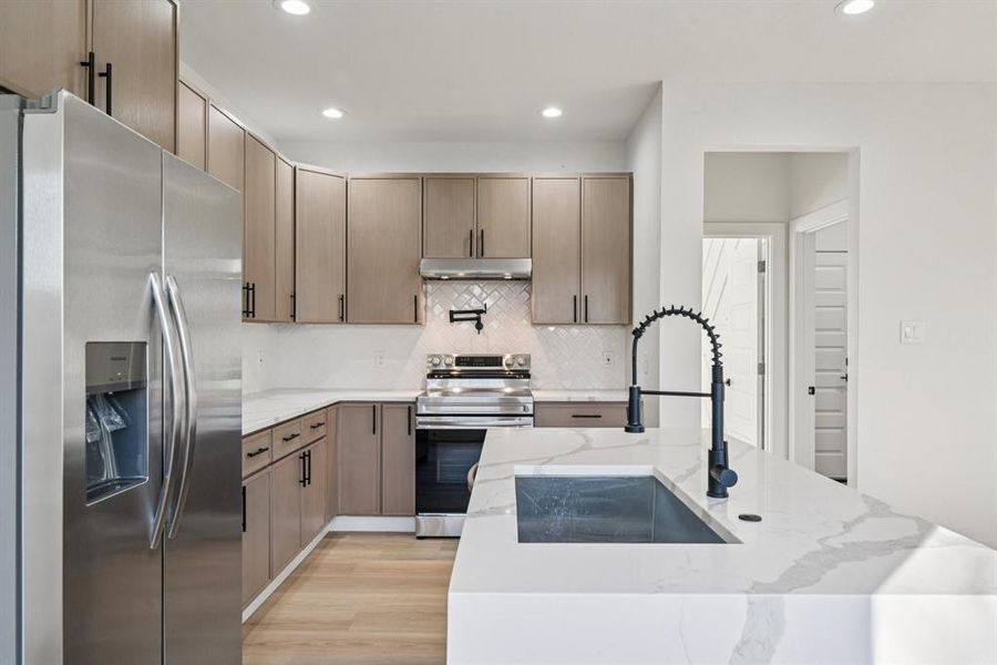 Kitchen featuring appliances with stainless steel finishes, light stone countertops, recessed lighting, tasteful backsplash, and light wood-style flooring