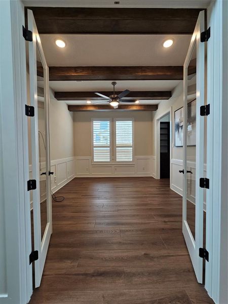 This photo showcases a room with elegant French doors, rich wood flooring, and exposed wooden ceiling beams. The space has a ceiling fan, recessed lighting, and a window with shutters, creating a bright, inviting atmosphere ideal for an office or study. This photo showcases a room with elegant French doors, rich wood flooring, and exposed wooden ceiling beams. The space has a ceiling fan, recessed lighting, and a window with shutters, creating a bright, inviting atmosphere ideal for an office or study.