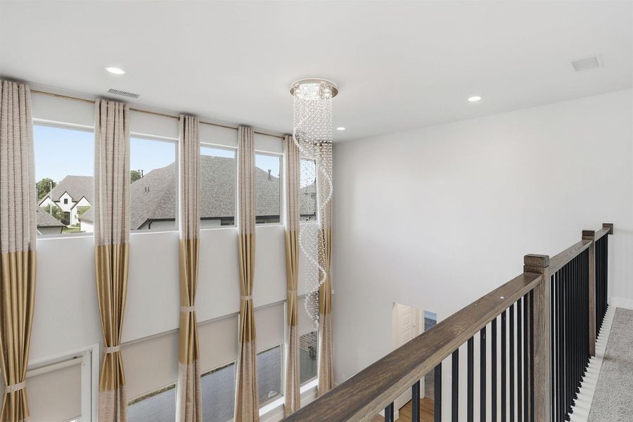 From the upstairs landing, oversized windows flood the home with natural light while the dramatic crystal chandelier provides an elegant focal point that beautifully connects both levels of the residence.