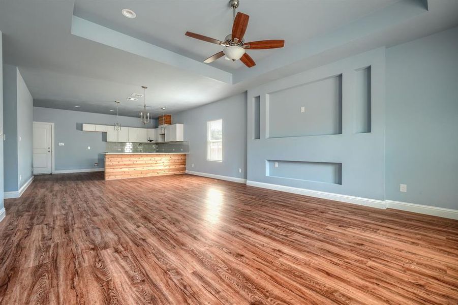 Unfurnished living room featuring a raised ceiling, ceiling fan, and hardwood / wood-style floors