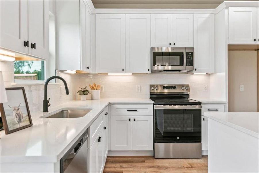 Modern kitchen featuring white shaker-style cabinetry with black hardware, stainless steel appliances, a white tile backsplash, and light-toned countertops